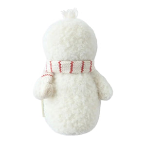The Cuddle + Kind Baby Snowman - Candy Cane, handcrafted from cotton yarn, faces away while wearing a white scarf with red stripes against a plain white background.