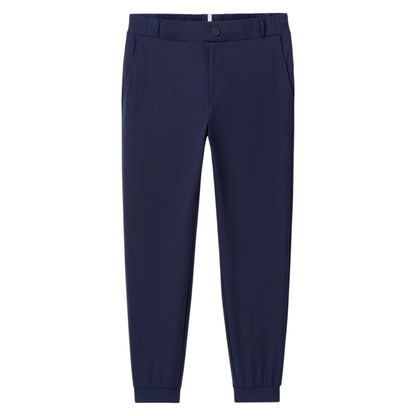 The Johnnie-O Solom Pant is a navy blue modern jogger with an elastic waistband, side pockets, and cuffed ankles, made from lightweight stretchy fabric and shown against a white background.