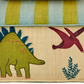 This vibrant bag, adorned with an embroidered green dinosaur, red pterosaur, and blue plant design, captures the essence of handmade artistry found in Madagascar creations. Its blue and green striped flap reflects the natural allure of materials used in products like the Rice Raffia Toy Basket from Rice.