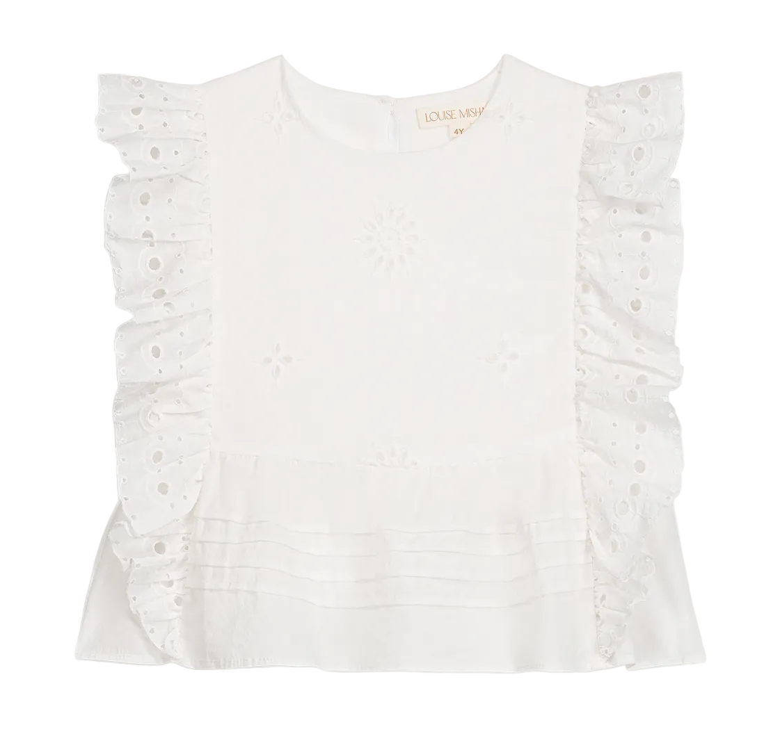 The Girls’ Esia Blouse by Louise Misha is a white cotton top featuring embroidered floral patterns, ruffled eyelet sleeves, delicate eyelet embroidery, a pleated hem, and a round neckline. The garment is displayed on a plain white background.