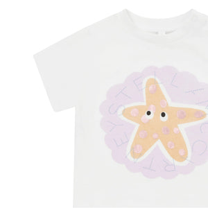 The Baby Girls' Starfish T-Shirt by Stella McCartney Kids features a pastel orange starfish with pink dots, cartoon eyes, and lavender text—making it a fun and playful beach shirt.