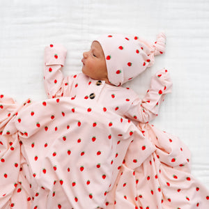 A newborn baby lies on a white blanket, dressed in the Lou Lou & Company Baby Girls’ and Girls’ Junie Top & Bottoms set, featuring a silky-soft strawberry print pattern.