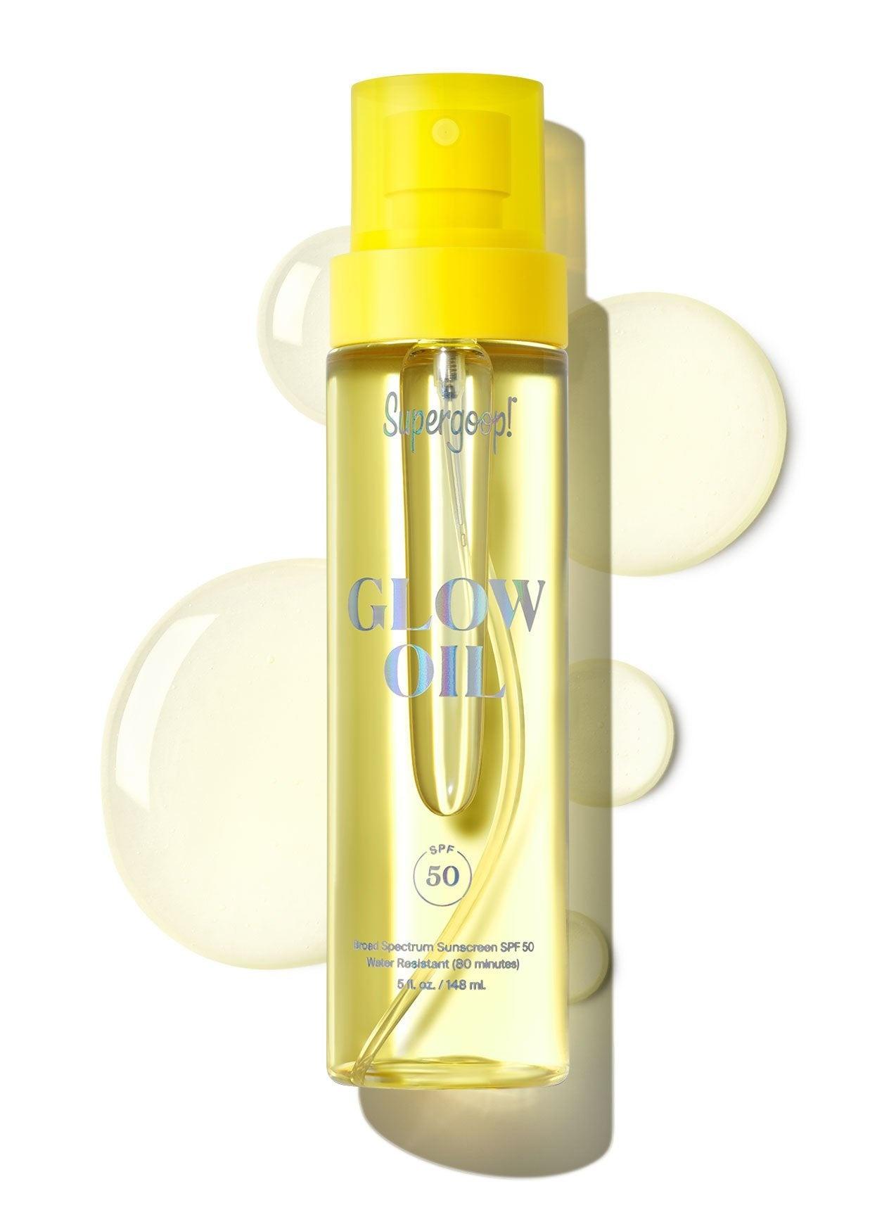 A bottle of Supergoop Glow Oil SPF 50, featuring a yellow cap and surrounded by droplets, highlights its antioxidant-rich formula. This body oil sunscreen delivers a radiant glow along with high protection.