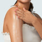 A person in a white sleeveless top applies Supergoop! Glowscreen Body SPF 40 to their arm, showcasing smooth, glowing skin.