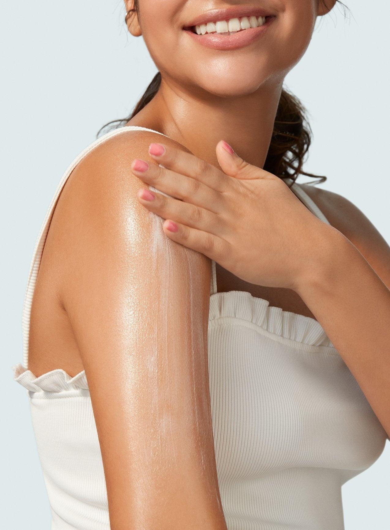 A person in a white sleeveless top applies Supergoop! Glowscreen Body SPF 40 to their arm, showcasing smooth, glowing skin.