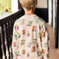 A child with short blonde hair stands on a balcony facing away, wearing the Arsene & Les Pipelettes Boys' and Girls' Mini Coco Sweatshirt with colorful prints and green pants.