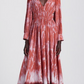 A person wearing the Altuzarra Kathleen Dress, a long-sleeved rust-red and white shibori maxi with a deep V-neckline and gathered waist.