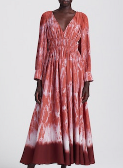 A person wearing the Altuzarra Kathleen Dress, a long-sleeved rust-red and white shibori maxi with a deep V-neckline and gathered waist.