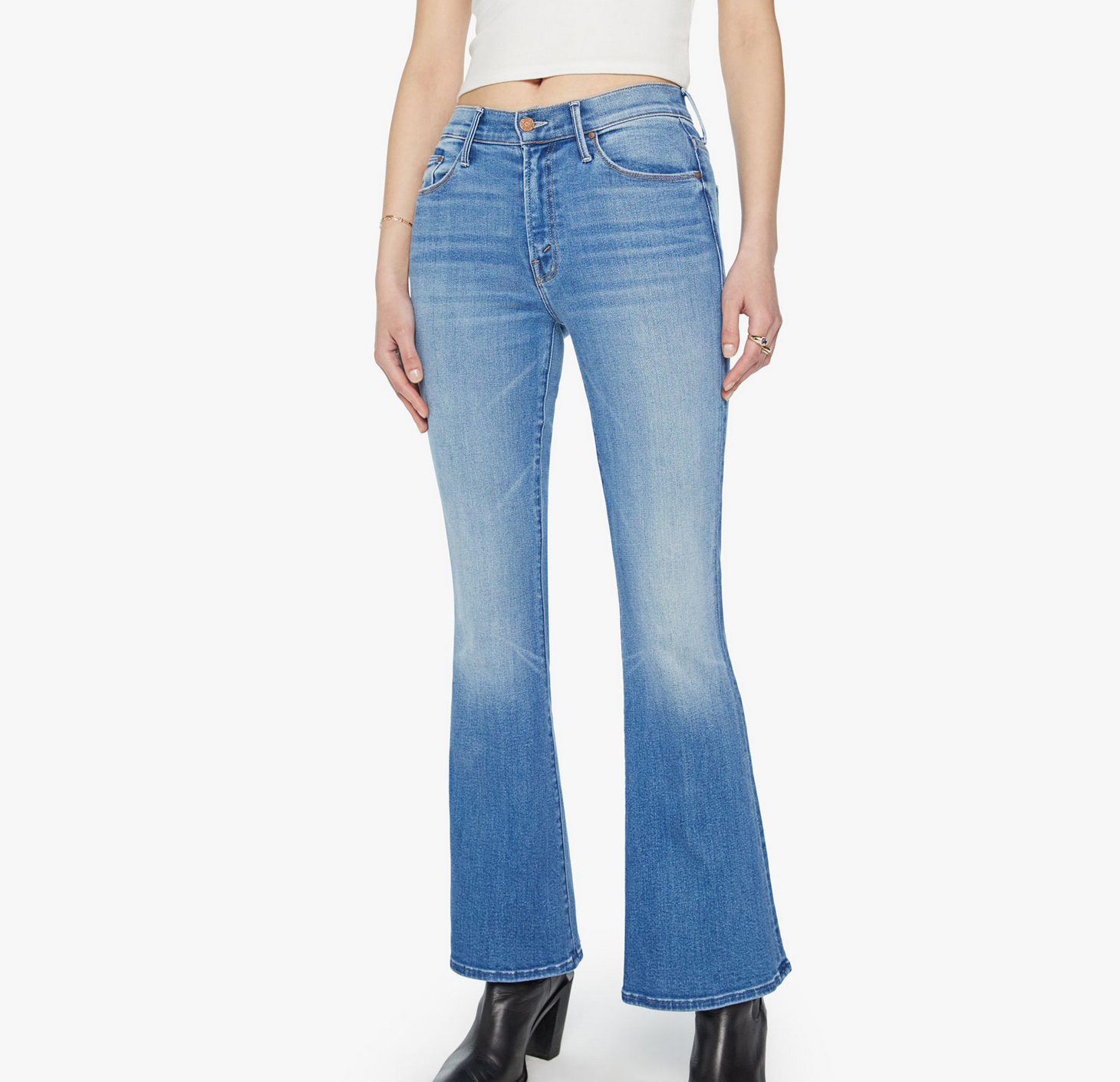 Person wearing Mother’s The Weekender light blue mid-rise flare jeans with stretch, paired with a white crop top and black boots, standing against a plain white background.