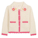 The Girls’ Josia Cardigan by Louise Misha is a cream cotton knit with pink trim, pink pocket accents, white button closure, and hand-crocheted flower details on the collar, displayed on a plain background.