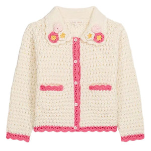 The Girls’ Josia Cardigan by Louise Misha is a cream cotton knit with pink trim, pink pocket accents, white button closure, and hand-crocheted flower details on the collar, displayed on a plain background.