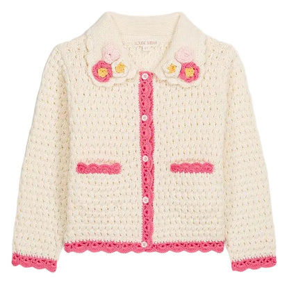 The Girls’ Josia Cardigan by Louise Misha is a cream cotton knit with pink trim, pink pocket accents, white button closure, and hand-crocheted flower details on the collar, displayed on a plain background.