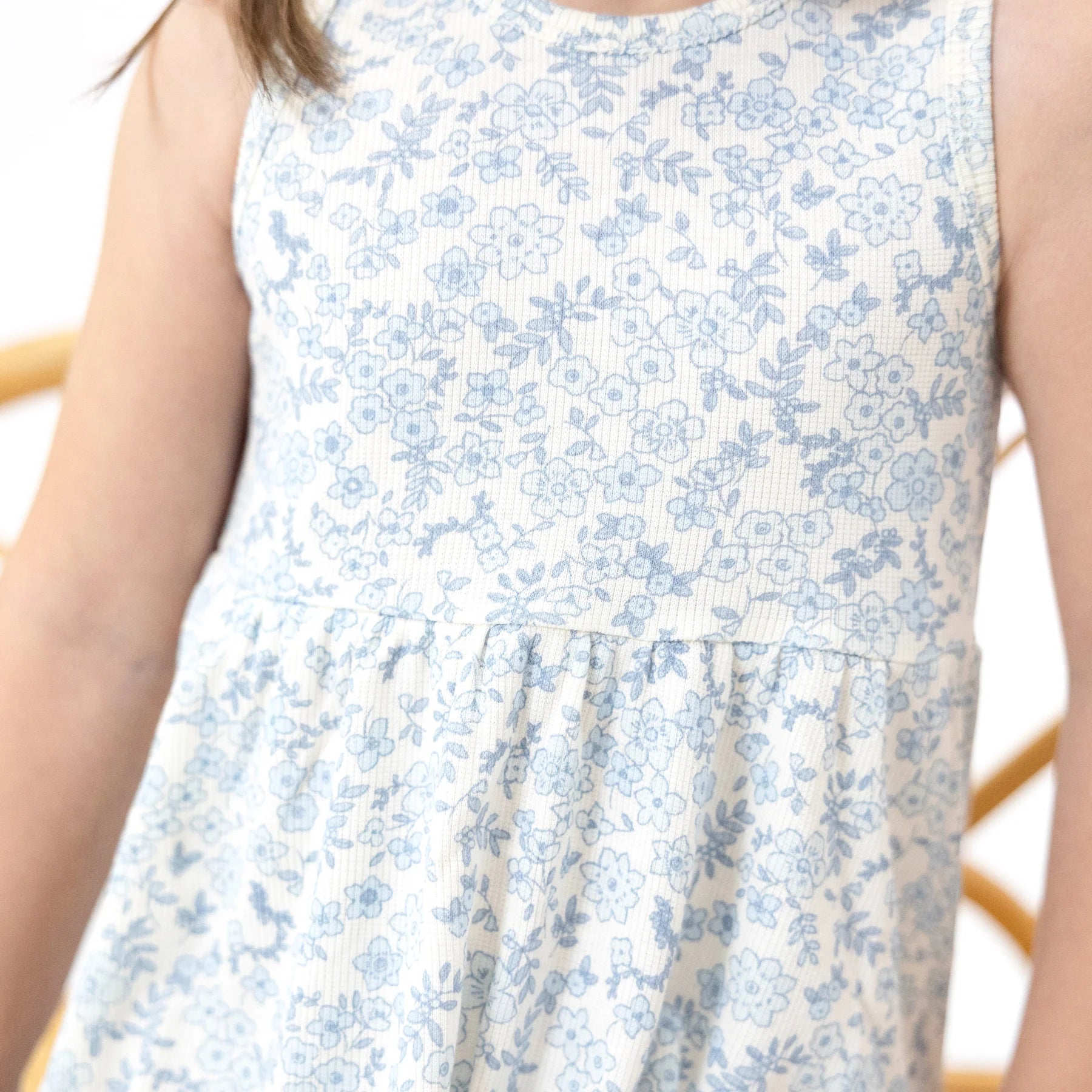 Close-up of the Angel Dear Baby Girls' and Girls' Ribbed Modal Tank Dress & Bloomer, featuring a light blue floral print on white. Child’s arms and upper body are partially shown. Available in toddler sizes.