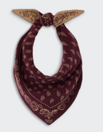 The Wild Rag by Guest in Residence is a maroon cotton-silk bandana featuring a beige paisley pattern, styled in a loose knot against a plain background. This best-selling accessory brings effortless elegance to any ensemble.