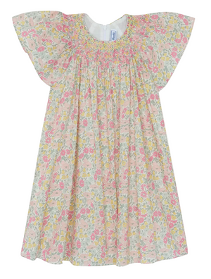 The Tartine et Chocolat Girls’ Liberty Print Dress is a short-sleeved, pastel-colored cotton dress for children, adorned with a delicate smocked collar and a charming Liberty print featuring pink, yellow, and green flowers on a white background.