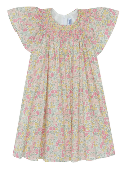 The Tartine et Chocolat Girls’ Liberty Print Dress is a short-sleeved, pastel-colored cotton dress for children, adorned with a delicate smocked collar and a charming Liberty print featuring pink, yellow, and green flowers on a white background.