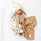 A baby dressed in Lou Lou & Company’s Baby Boys’ and Boys’ Teddy Top & Bottoms, featuring a silky-soft bear pattern with built-in footies and a matching hat, sleeps on a white blanket while holding a tan textured blanket and using a pacifier.