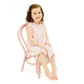 A young girl with brown hair, barefoot and wearing the Angel Dear Jill Peter Pan Button Front Dress with Ric-Rac Trim and Diaper Cover, sits on a pink chair against a white background.