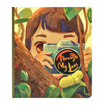 The illustrated book cover showcases a budding photographer amidst lush foliage, holding a camera that features "Kidamento Through My Lens" elegantly written on the lens cap. It's an ideal choice for a children's photography book or for those interested in exploring Kidamento cameras.