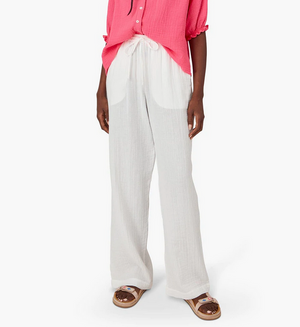 Someone styled in a pink top with Xirena's Dylan Pant, featuring white washed cotton gauze and an elastic drawstring waist, paired stylishly with sandals.