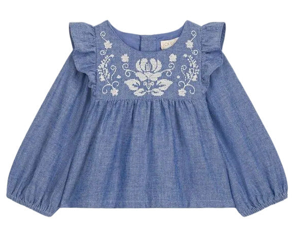 The Louise Misha Baby Girls’ Mikani Set features a blue long-sleeve cotton Oxford blouse with ruffled shoulders and white floral embroidery on the chest, shown on a white background—a charming piece from our embroidered baby outfit collection.