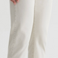 A person wears light beige Tellis Selvage jeans by AG Jeans, cuffs rolled up, shown mid-torso to feet against a plain background. Made from Japanese stretch selvage denim for both style and comfort.