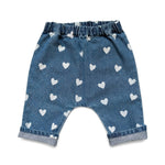 The Louis Louise Baby Girls’ Jungle Trouser features blue denim with an elastic waistband, a delightful white heart print, and rolled cuffs, displayed against a white background.