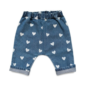 The Louis Louise Baby Girls’ Jungle Trouser features blue denim with an elastic waistband, a delightful white heart print, and rolled cuffs, displayed against a white background.