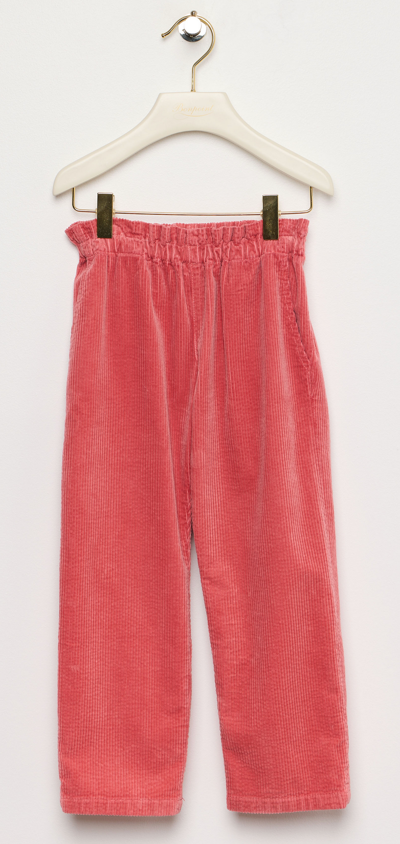 The Girls’ July Pants by Bonpoint, crafted from organic cotton in coral pink with a straight-cut silhouette and an elastic waistband, are displayed on a white hanger against a plain white background—perfect for girls.
