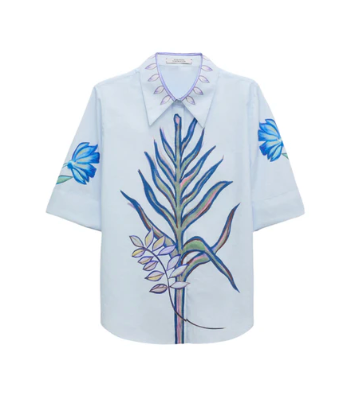 The Floral Embrace Blouse by Dorothee Schumacher is a light blue classic shirt with short sleeves, showcasing a large botanical key print on the front and blue flower designs on each sleeve.
