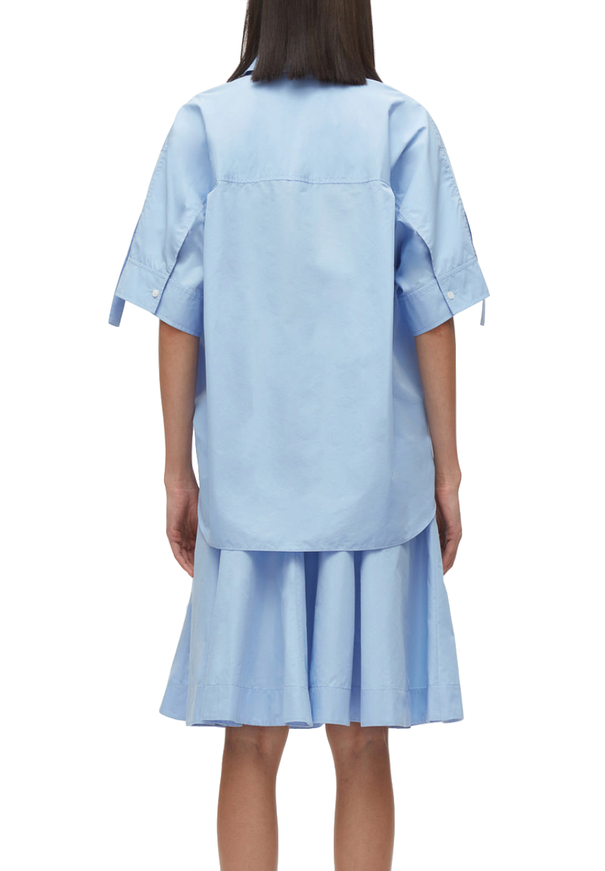 Woman standing with her back to the camera wearing a blue 3.1 Phillip Lim Tucked Front Shirt Dress made of Japanese poplin with an oversized fit and short sleeves.