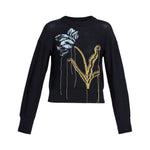The Erdem Floral Crew Neck Jumper is a black merino wool long-sleeve with an intarsia-knitted abstract blue and white flower and gold stems on the front, creating a bold tulip-inspired design.
