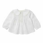 The Baby Girls’ Ester Tunic by Louis Louise is a white, long-sleeved blouse made from soft cotton voile fabric, featuring a lace-trimmed collar, delicate front pintuck detailing, and three buttons.