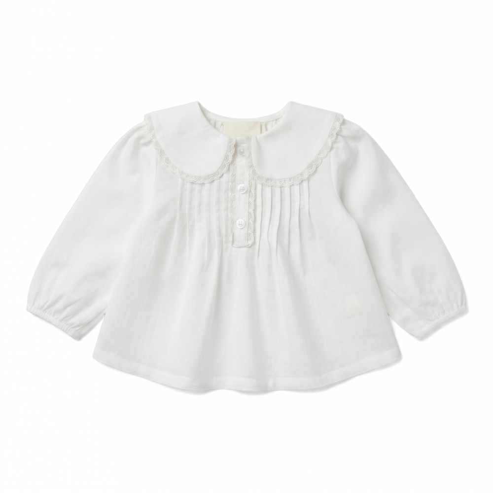 The Baby Girls’ Ester Tunic by Louis Louise is a white, long-sleeved blouse made from soft cotton voile fabric, featuring a lace-trimmed collar, delicate front pintuck detailing, and three buttons.