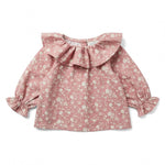 The Baby Girls’ Lilie Shirt by Louis Louise features a baby pink color with a white floral print, long sleeves, ruffled collar, and ruffled cuffs. The blouse is displayed laid flat on a white background.