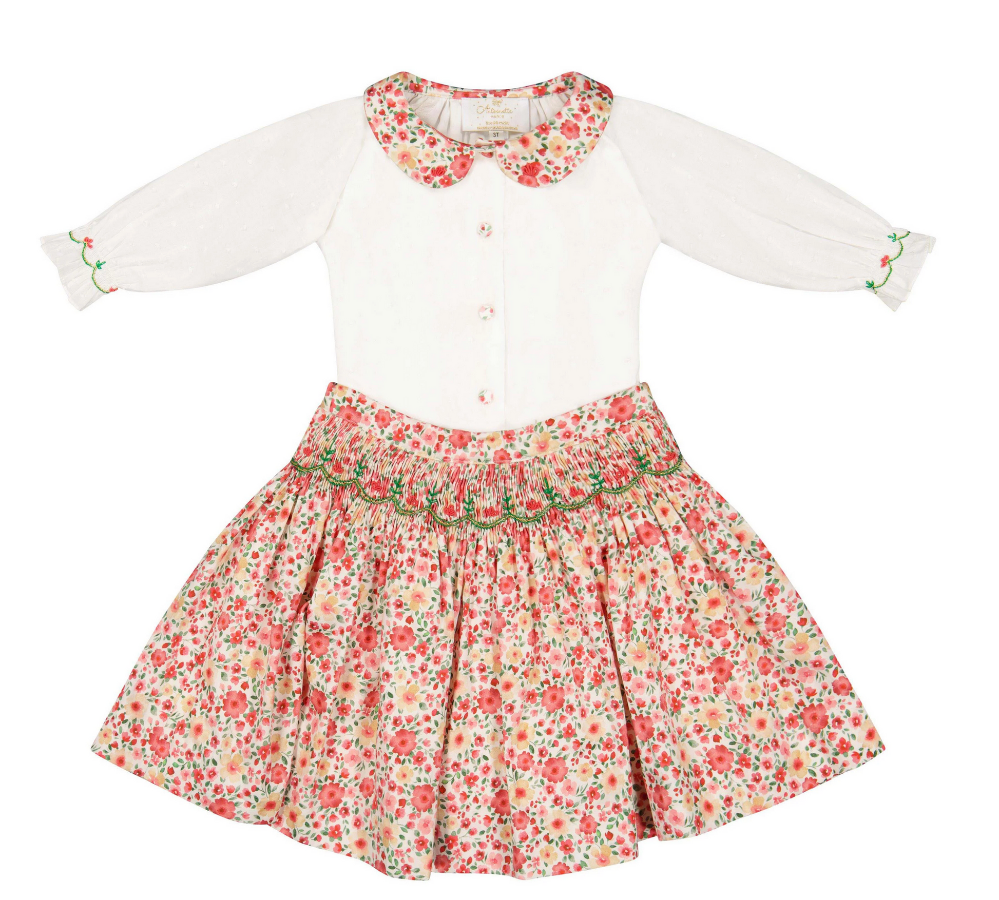The Antoinette Girls' Marie Red Floral Smocked Skirt and Blouse Set features a white long-sleeve embroidered collar blouse and a red floral skirt—an ideal girls’ holiday outfit with delicate waist detail.