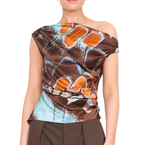 A woman wearing the Staud Phare Silk Top—a brown one-shoulder silk satin piece adorned with orange and blue abstract patterns and a drapey fitted silhouette—paired with brown pants.