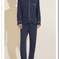 A person stands barefoot in the Eberjey Willam Long PJ Set—a matching navy blue men's pajama set with white piping, made from soft TENCEL™ Modal and featuring a long-sleeve button-up top and pants for temperature regulation.