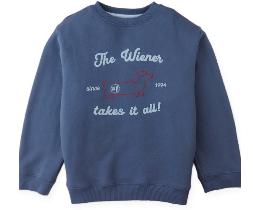 The Boys’ Riccardo Pullover by Gingersnaps is a blue fleece sweatshirt, detailed with a snug and stylish red embroidered outline of a dachshund and the phrase “The Wiener takes it all! since 1994” on the front.