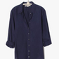 A navy blue Xirena Beau Shirt, with long sleeves and button-up style, hangs elegantly on a hanger against a plain background, showcasing the classic charm of cotton poplin.