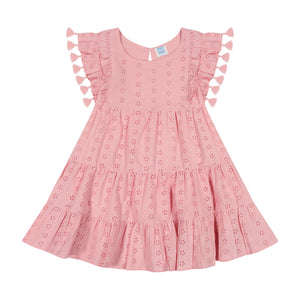 The Girls’ Sophie Tassel Dress by Mer is a pink, short-sleeved dress for girls made from lightweight cotton, featuring tiered layers with eyelet details and flutter sleeves accented by playful tassels, shown laid flat on a white background.