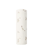 A Quincy Mae Swaddle made from rolled organic jersey white fabric, adorned with small animal and floral prints, is displayed upright against a plain white background.