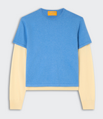 The Guest in Residence Layer Tee, in blue cotton-cashmere, is styled over a long-sleeve cream shirt for a modern layered look against a simple light background.