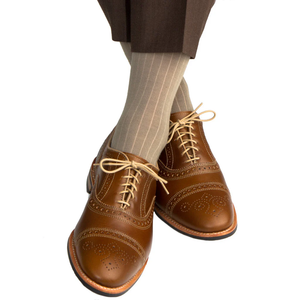 A person wearing brown dress shoes, brown pants, and Dapper Classics Taupe Solid Ribbed Mid Calf Socks with legs crossed against a white background.