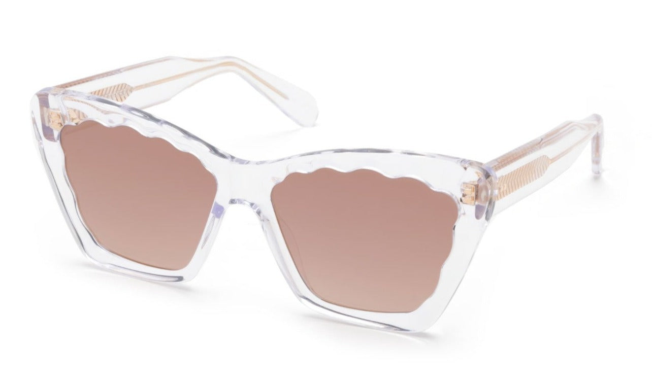 Krewe Brigitte Sunglasses by Krewe are clear-framed luxury eyewear with pink-tinted lenses, a scalloped edge design, and a chic cat-eye silhouette, offering full UVA/UVB protection.