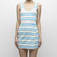 A woman wears the Simkhai Marston Striped Mini Dress, featuring blue and white horizontal nautical stripes and a sleeveless scoop-neck design, as she stands against a plain background.