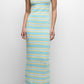 A woman wears the Simkhai Connelly Striped Midi Dress—a slim-fit, sleeveless, ankle-length knit dress with blue, yellow, and white stripes and a ribbed square neckline—paired with white sandals against a plain background.
