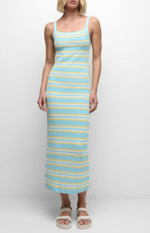 A woman wears the Simkhai Connelly Striped Midi Dress—a slim-fit, sleeveless, ankle-length knit dress with blue, yellow, and white stripes and a ribbed square neckline—paired with white sandals against a plain background.