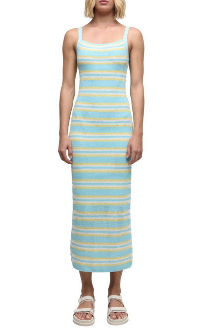 Wearing the Simkhai Connelly Striped Midi Dress—an ankle-length, sleeveless knit dress with blue, yellow, and white stripes, a ribbed square neckline, and slim fit—paired with white sandals.