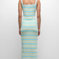 Person stands with back to camera, wearing the Simkhai Connelly Striped Midi Dress featuring blue, yellow, and white stripes, a ribbed square neckline, and slim fit, paired with white sandals against a plain white background.